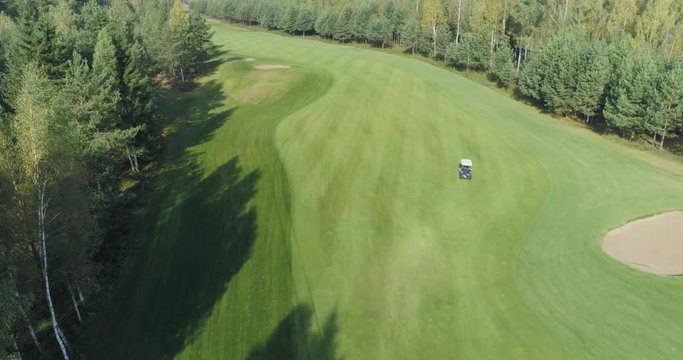 Summer sunny day, aerial view of Golf course in forest area, Golf Club, electric golf car rides on the lawn, view of the field of green lawn near the forest.