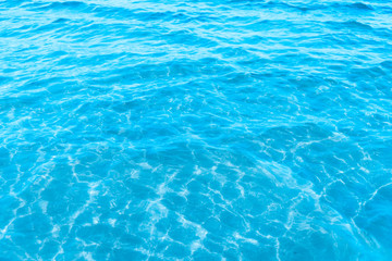 Naklejka na ściany i meble Blue transparent sea water near the beach texture background. clear water surface with slight waves and glare on a sunny day. sea ​​vacation