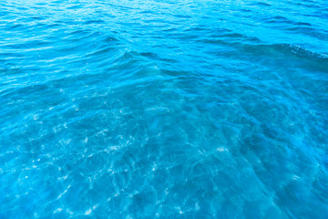Blue transparent sea water near the beach texture background. clear water surface with slight waves and glare on a sunny day. sea ​​vacation