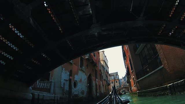 View from boat or gondola which going under old bridge at the narrow slums in the antique district in Venice, Italy.