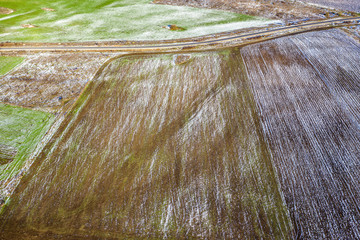 Fields with winter crops and plowed field. Fields covered with snow. Aerial view.