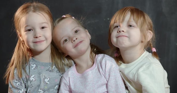 Three cute babies of five years of age laugh and hug while looking at the camera.