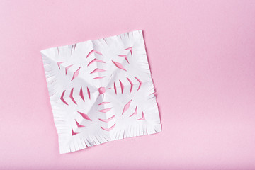 Snowflake cut out of paper on a pink background. Children's creativity.