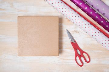 Preparation for the holiday. Gift wrapping. Cardboard box, wrapping paper and scissors on a wooden background. Top view