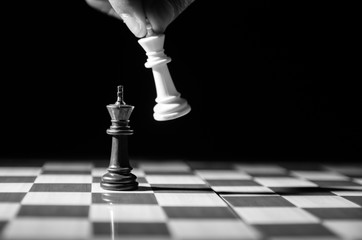 Black and white image of white king about to take down black king. Hand and fingers and chess board