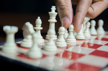 Close up on fingers and hand on white chess pieces on chess board. Fingers on white pawn e2 to play move e4 or e3 in chess