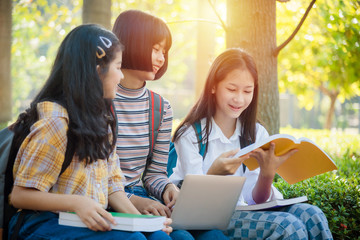 Three asian teenager student sitting in park and using notebook computer for doing homework together