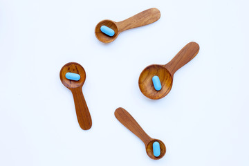 Medical blue pills with wooden spoon on white background.