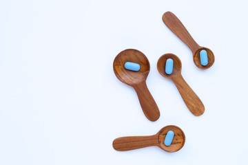 Medical blue pills with he wooden spoon on white background.