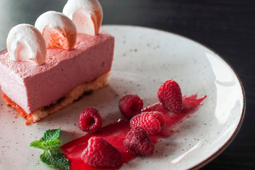 Tasty raspberry dessert cheesecake with berries, mint and marshmallows on a plate on a wooden background