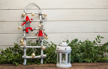 Little dwarf dolls are sitting on the Christmas stairs. White wooden background and decorative lights
