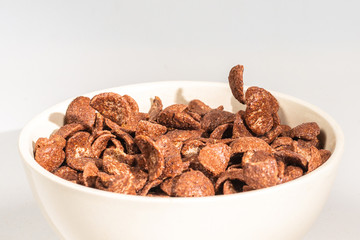 Chocolate corn flakes falling to the white bowl isolated on white. Motion.