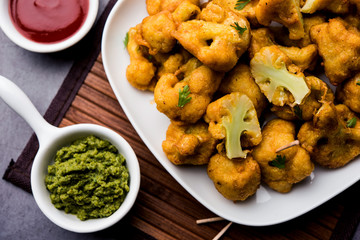 Gobi pakora or Phoolgobi pakoda made using fresh cauliflower dipped chickpea batter and then fried in oil. served with tomato ketchup and mint chutney. selective focus