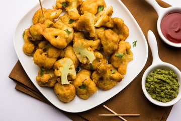 Gobi pakora or Phoolgobi pakoda made using fresh cauliflower dipped chickpea batter and then fried in oil. served with tomato ketchup and mint chutney. selective focus