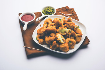 Gobi pakora or Phoolgobi pakoda made using fresh cauliflower dipped chickpea batter and then fried in oil. served with tomato ketchup and mint chutney. selective focus
