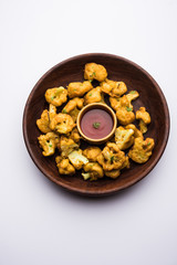 Gobi pakora or Phoolgobi pakoda made using fresh cauliflower dipped chickpea batter and then fried in oil. served with tomato ketchup and mint chutney. selective focus