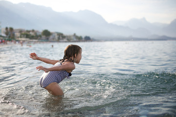 child splashes water on pebble beach in Turkey