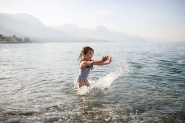 child splashes water on pebble beach in Turkey