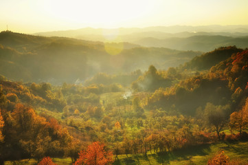 Beautiful autumn mountain in the sunset mist. Glowing sunset on the autumn forest. Lens flare effect. Soft focus.