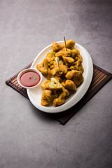 Gobi pakora or Phoolgobi pakoda made using fresh cauliflower dipped chickpea batter and then fried in oil. served with tomato ketchup and mint chutney. selective focus