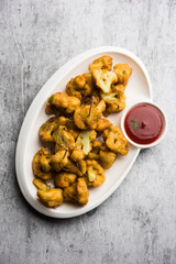 Gobi pakora or Phoolgobi pakoda made using fresh cauliflower dipped chickpea batter and then fried in oil. served with tomato ketchup and mint chutney. selective focus