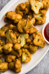 Gobi pakora or Phoolgobi pakoda made using fresh cauliflower dipped chickpea batter and then fried in oil. served with tomato ketchup and mint chutney. selective focus