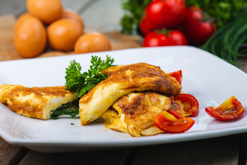Traditional omelet with vegetables, spinach, tomatoes and herbs on a wooden table in a restaurant.
