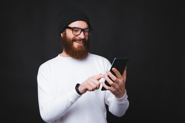 Portrait of happy trendy bearded man using his tablet over dark background