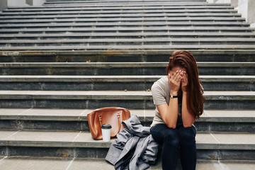 Sad depressed young woman covering face with hands when sitting on steps and crying over lost...
