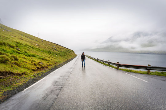 Adventuristic travel photo with male traveller walking by empty road of Faroe Islands.