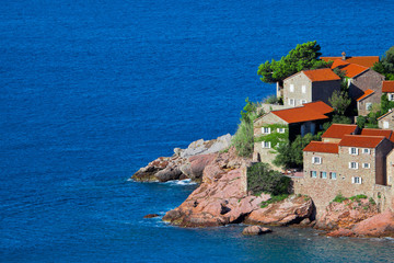 Cute fishing village.  houses with a tiled roof and green trees by the blue sea. happiness in relaxation in warm countries. Sveti Stefan