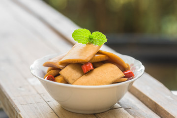 A bowl of sour radish slices sits on an old wooden board, decorated with a mint leaf.
