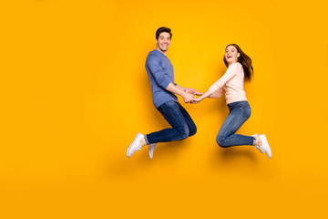 Fototapeta na wymiar Full size photo of cheerful crazy two people spouse relax rest fun jump hold hand wear blue pink sweater denim jeans sneakers isolated over bright shine color background