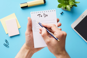 Male hands making a to-do list in a notebook over an office desk - obrazy, fototapety, plakaty