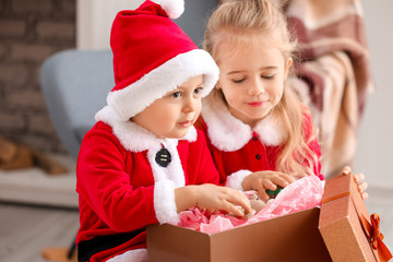 Cute little children in Santa costumes and with Christmas gift at home