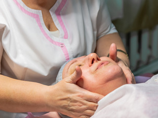 Fototapeta na wymiar A cosmetic procedure with manual facial massage in a beauty salon is performed for an aged woman. Improving skin turgor, rejuvenation and healing.