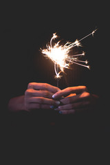 Holding sparklers stick on fire with both hands, on black background at night time in toning