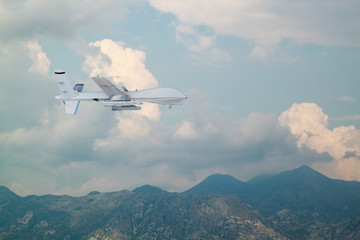 Spy unmanned aerial vehicle (UAV) flies over low mountains in mist with white clouds on blue sky...