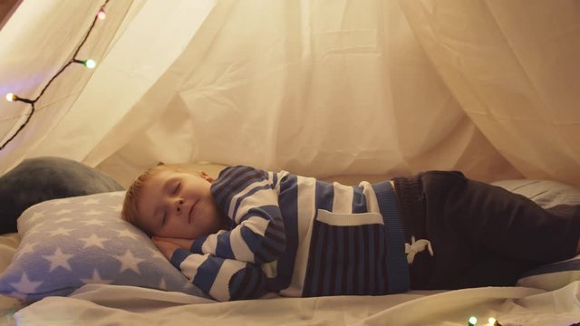 Little boy sleeping in children's tent at home. Happy caucasian kid in the playroom.