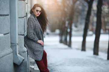 A woman stands on the street in winter near a building with white walls.