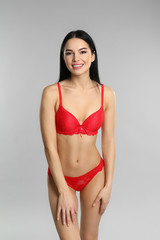 Fototapeta premium Beautiful young woman in red underwear on grey background