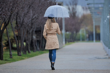 a girl walking through a park, with a transparent umbrella, is on her back