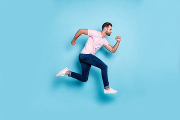 Fototapeta na wymiar Full length profile photo of attractive guy jumping high sportive competitions participant wear casual pink t-shirt jeans sneakers isolated blue color background
