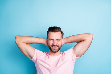 Fototapeta na wymiar Photo of attractive guy holding hands behind head enjoy amazing weekend day relaxing refreshment moment wear casual pink t-shirt isolated blue color background