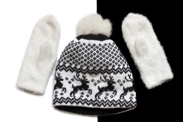 knitted white mittens and hat with Christmas pattern on black and white background flat lay
