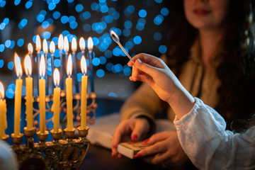 jewish holiday Chanukah/Hanukkah family selebration. Jewish festival of lights. Children lighting candles on traditional menorah over glitter shiny background - obrazy, fototapety, plakaty