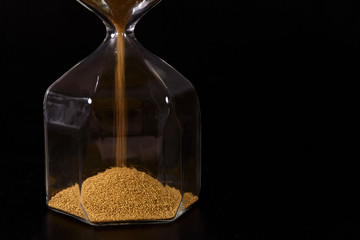 Modern hourglass with yellow sand on black background, close-up, copy space.  Time limit concept.