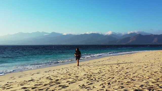lonely traveler walking along the sandy beach. Foamy waves washing the sand, mountain range in the background