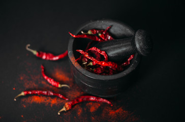 Dry red spicy peppers and powder in stone mortar. Dark photo, copy space.