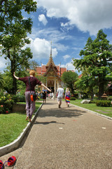 A young girl walks barefoot along the curb to a Buddhist temple. In the background is a white building with red and gold trim. Traditional pagoda.